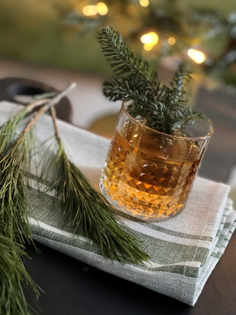 Holiday cocktail in glass with evergreen sprig flourishes.