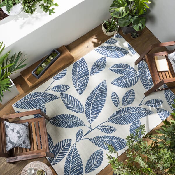 birds-eye view of a cream colored rug with blue leaf print surrounded by 2 outdoor chairs and planters