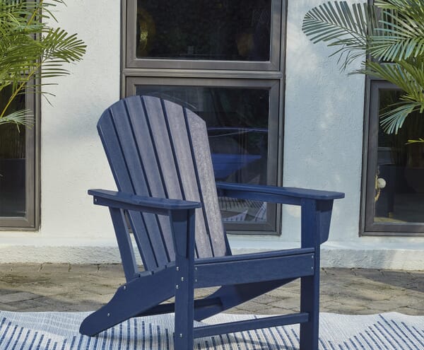 a blue adirondack chair on top of a rug outside with plants on each side
