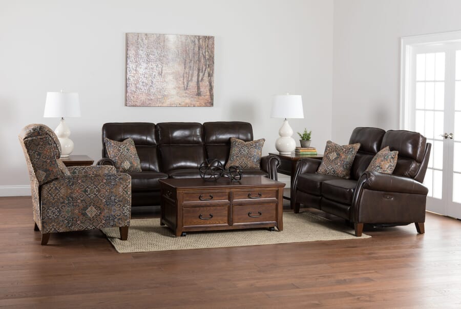 Brown leather sofa and loveseat with orange print pillows and matching orange print chair in living room setting