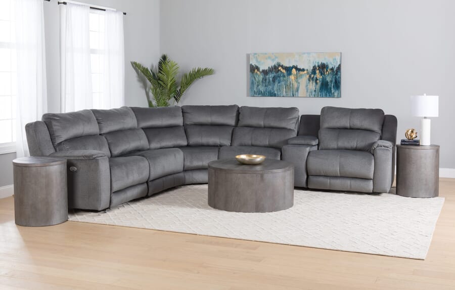 Gray reclining sectional with gray wood tables and beige rug in living room setting.