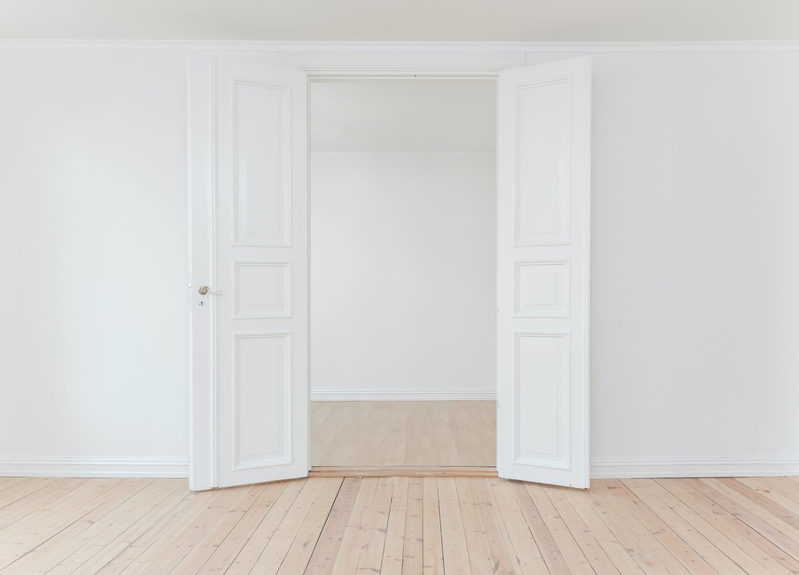 Empty room with wood floors and two white 3 panel doors open