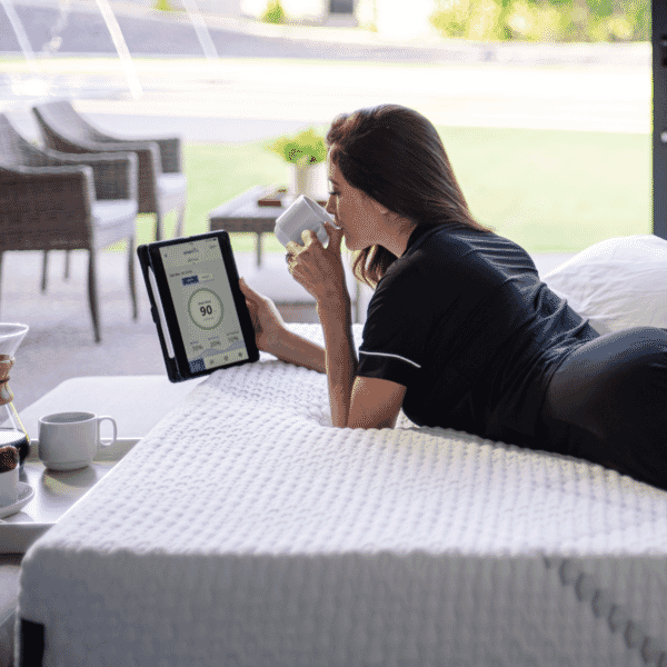 Lady laying on her stomach on a Smart Life by King Koil mattress sipping coffee with tablet in hand.